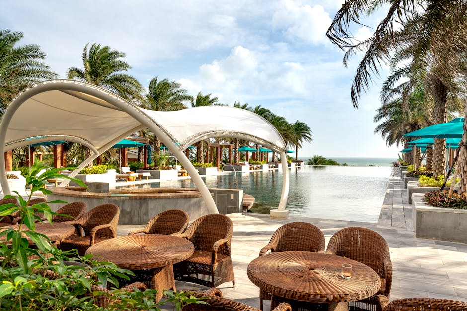 Luxurious tropical resort poolside with palm trees, wicker chairs, and ocean view.