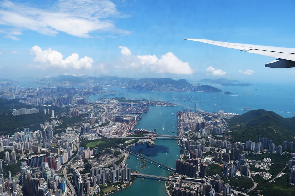 Stunning aerial view over Hong Kong with cityscape and ocean, featuring an airplane wing.