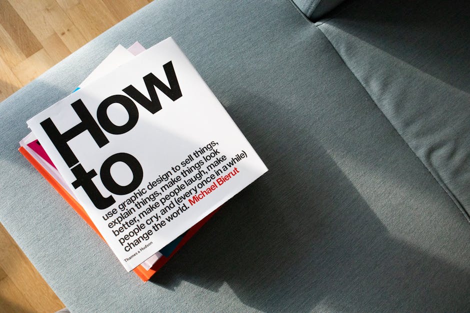 A collection of design books on a couch, showcasing 'How to' by Michael Bierut