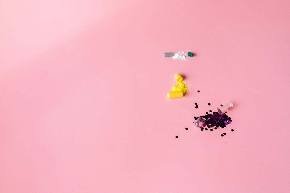 Close-up flat lay of colorful capsules and powders on pink surface with copy space.