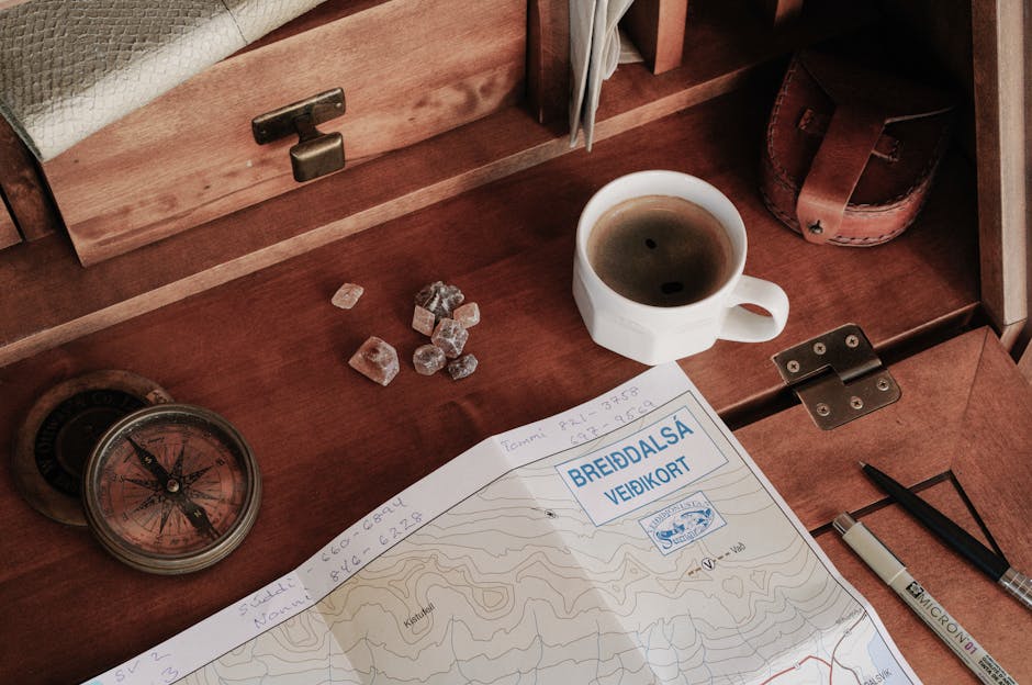 A top-down view of a rustic workspace featuring a map, compass, and a cup of coffee.