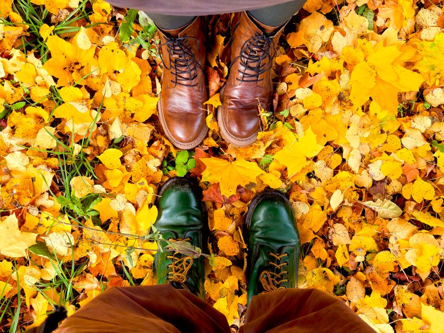 Overhead view of two pairs of boots on a bed of vibrant autumn leaves.